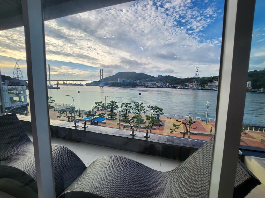 a view of the water from a window with chairs at Suite Stay Yeosu in Yeosu