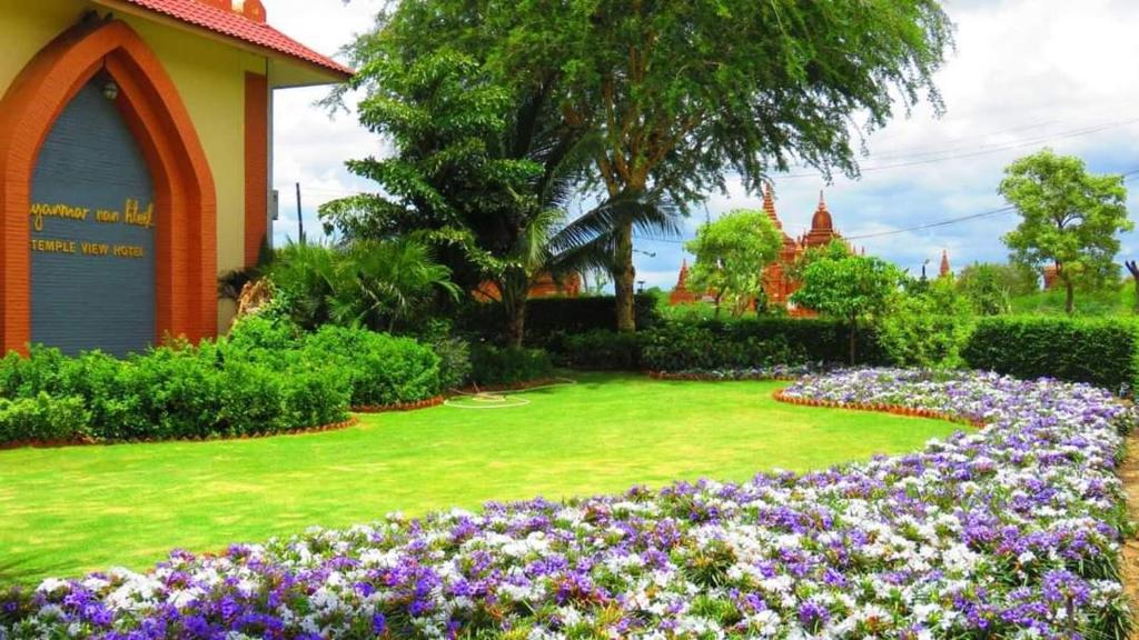 a garden with purple flowers in front of a building at Myanmar Nan Hteik Temple View Hotel in Bagan
