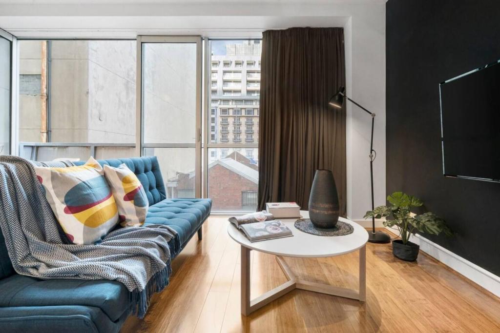 a living room with a blue couch and a table at 'Collins Central' Sleek Light-filled Pad in the CBD in Melbourne