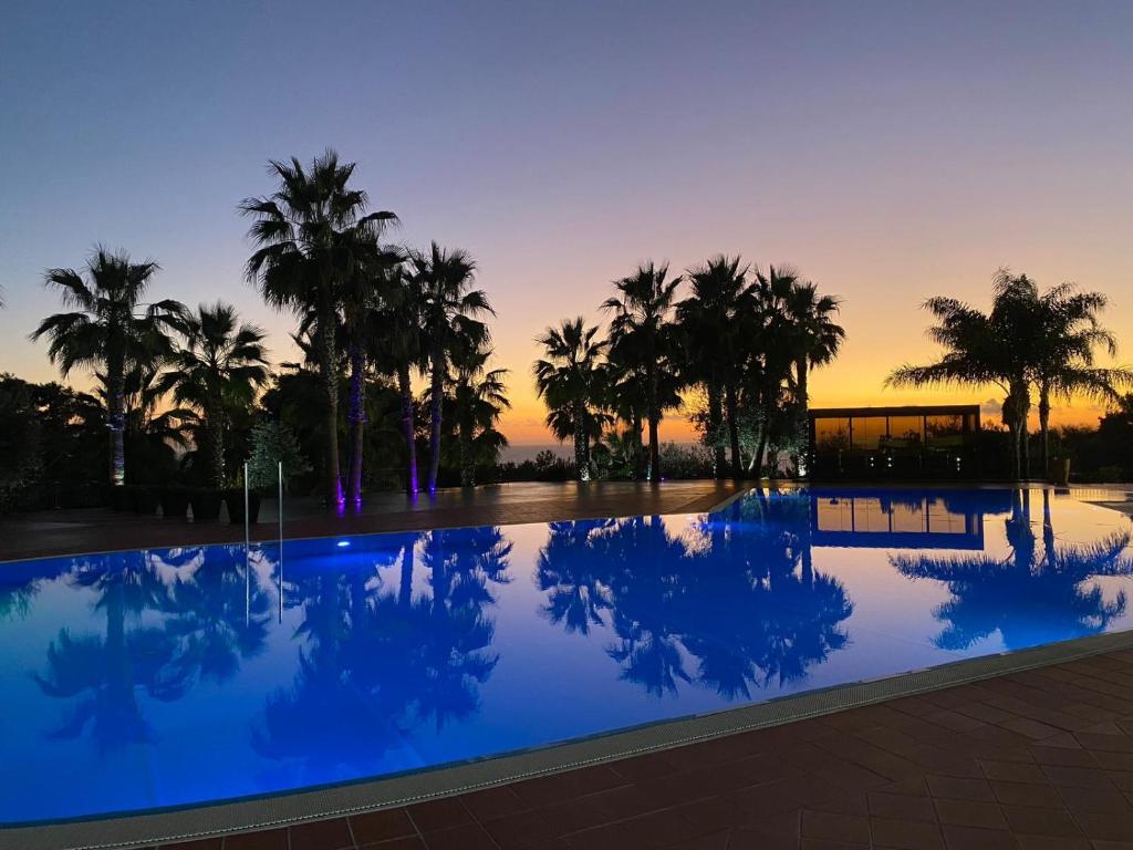 une piscine avec des palmiers et un coucher de soleil en arrière-plan dans l'établissement Baia Di Ulisse Wellness & Spa, à San Leone