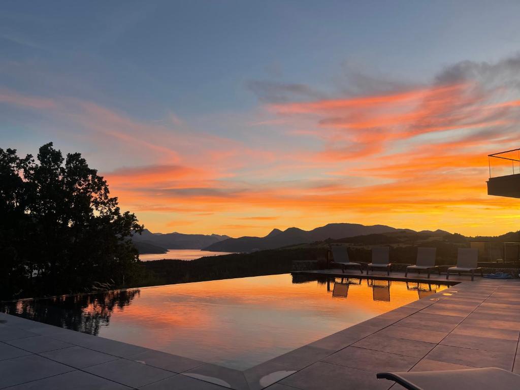 um pôr-do-sol sobre uma piscina com montanhas ao fundo em Les Restanques du lac em La Chapelle