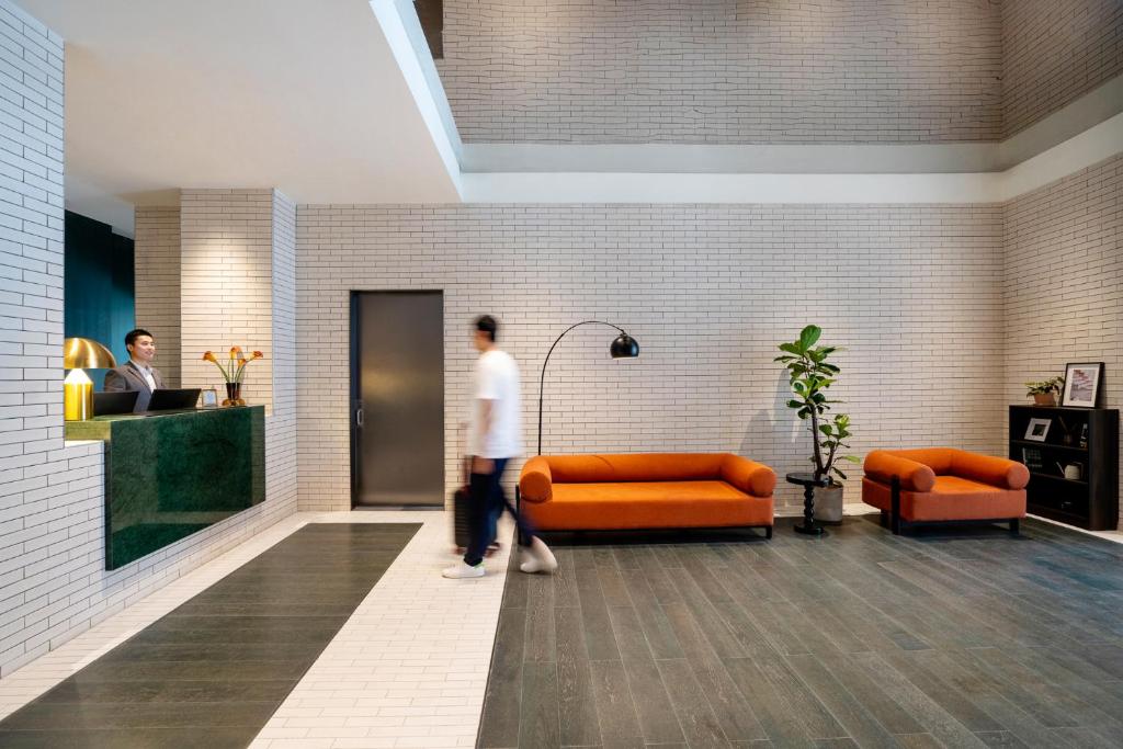 a man walking through a lobby with orange furniture at base-Beijing Wangfujing Serviced Apartment- in Hutong &Bike rental &Close to Forbidden City, Tian'anmen Square &Subway nearby &Free coffee &Washing machine,Kitchen &Restaurant discount &English speaking &High speed free WiFi in Beijing