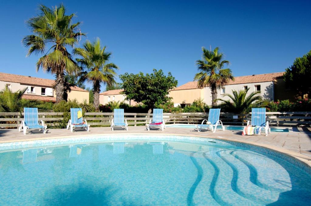 - une piscine avec des chaises bleues et des palmiers dans l'établissement Résidence Odalys Le Grand Bleu, à Vendres-Plage