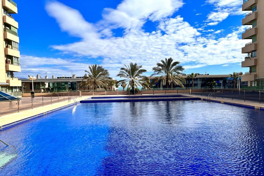 een groot zwembad met palmbomen en een blauwe lucht bij Apartamento dos habitaciones primera línea de playa in Valencia