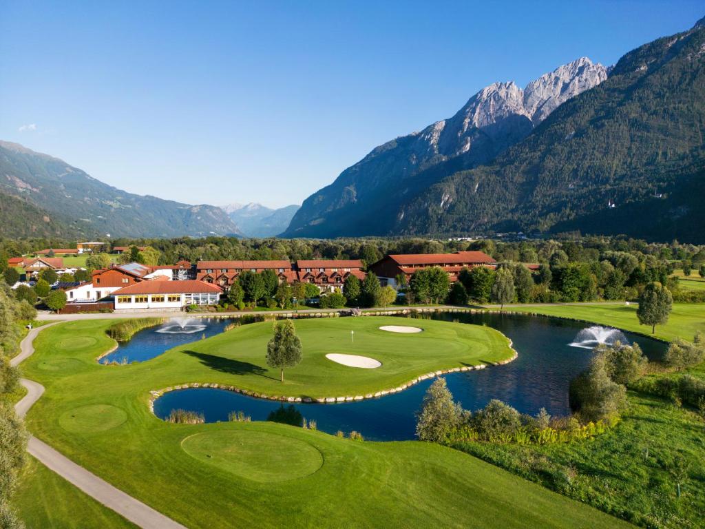 einen Golfplatz mit See und Bergen im Hintergrund in der Unterkunft Dolomitengolf Hotel & Spa in Lavant