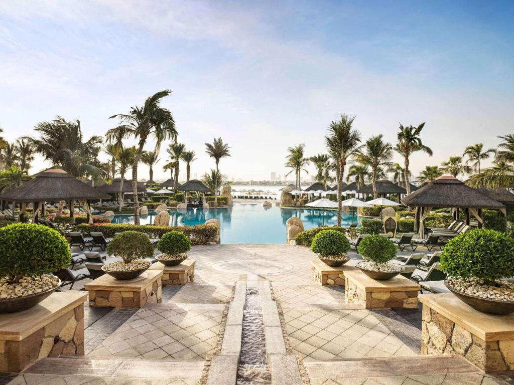 ośrodek z basenem, krzesłami i palmami w obiekcie Sofitel Dubai Palm Apartments w Dubaju