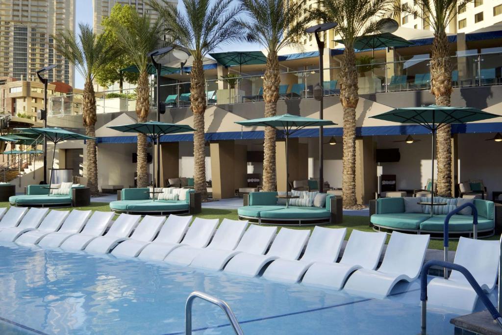 ein Pool mit Stühlen und Sonnenschirmen und Palmen in der Unterkunft Hilton Club Elara Las Vegas in Las Vegas