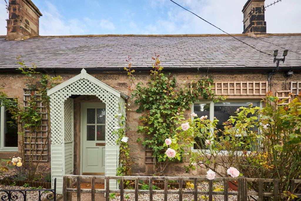 een stenen huis met een groene deur en rozen bij Host & Stay - The Old Post Office in Chatton