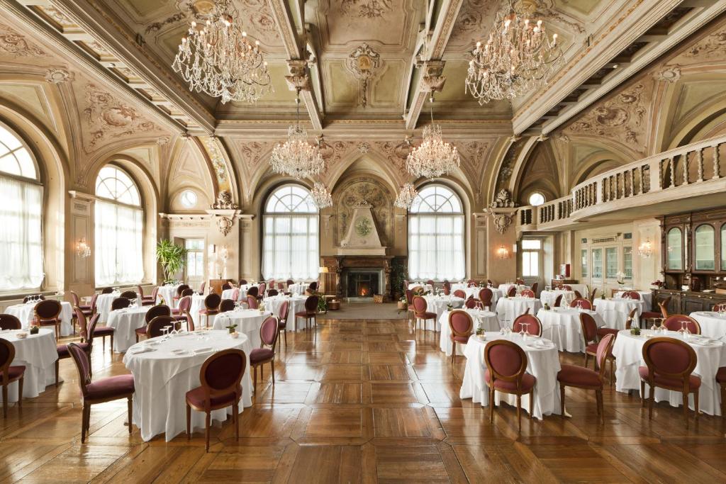 un comedor con mesas y sillas blancas y lámparas de araña en QC Terme Grand Hotel Bagni Nuovi, en Bormio