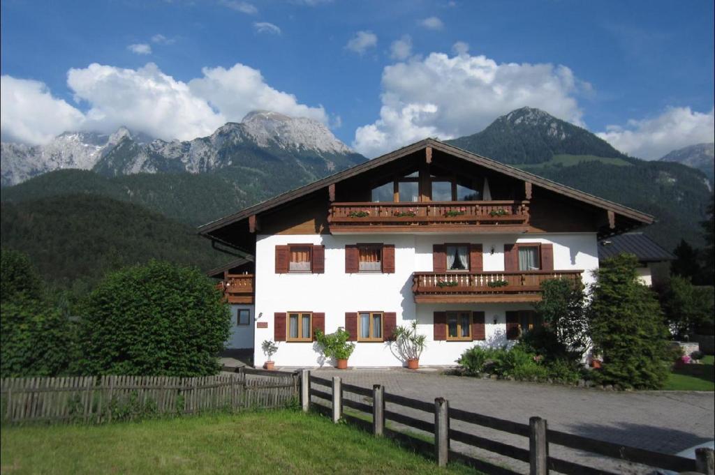 Une grande maison blanche avec des montagnes en arrière-plan dans l'établissement Ferienwohnungen Artenreitwinkl Hallinger, à Schönau am Königssee