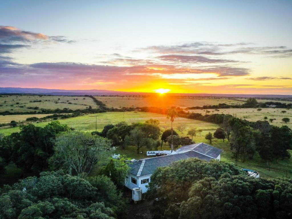 una casa en un campo con la puesta de sol en el fondo en Land's End Private Game Reserve, en Grahamstown