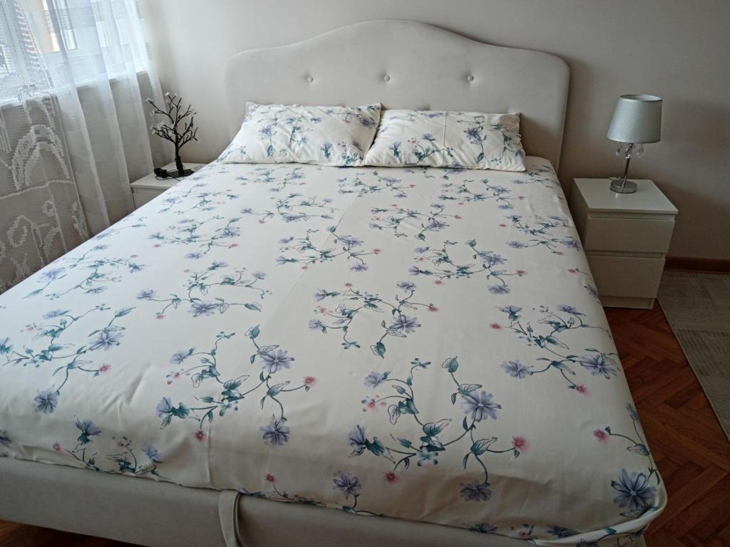 a bed with a white bedspread with blue flowers on it at Red Square Apartment in Pirot