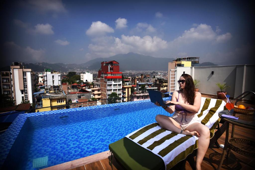 Divine Kathmandu Hotel في كاتماندو: امرأة تجلس على كرسي مع جهاز كمبيوتر محمول بجوار حمام السباحة