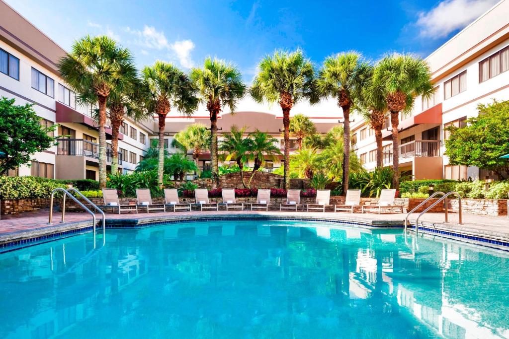uma piscina num hotel com cadeiras e palmeiras em Sheraton Suites Orlando Airport Hotel em Orlando