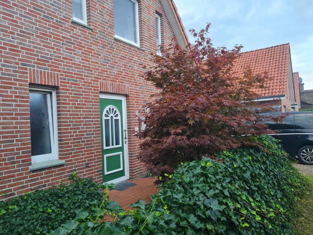 a red brick house with a green door and a tree at Delphin Monteurwohnung in Heede