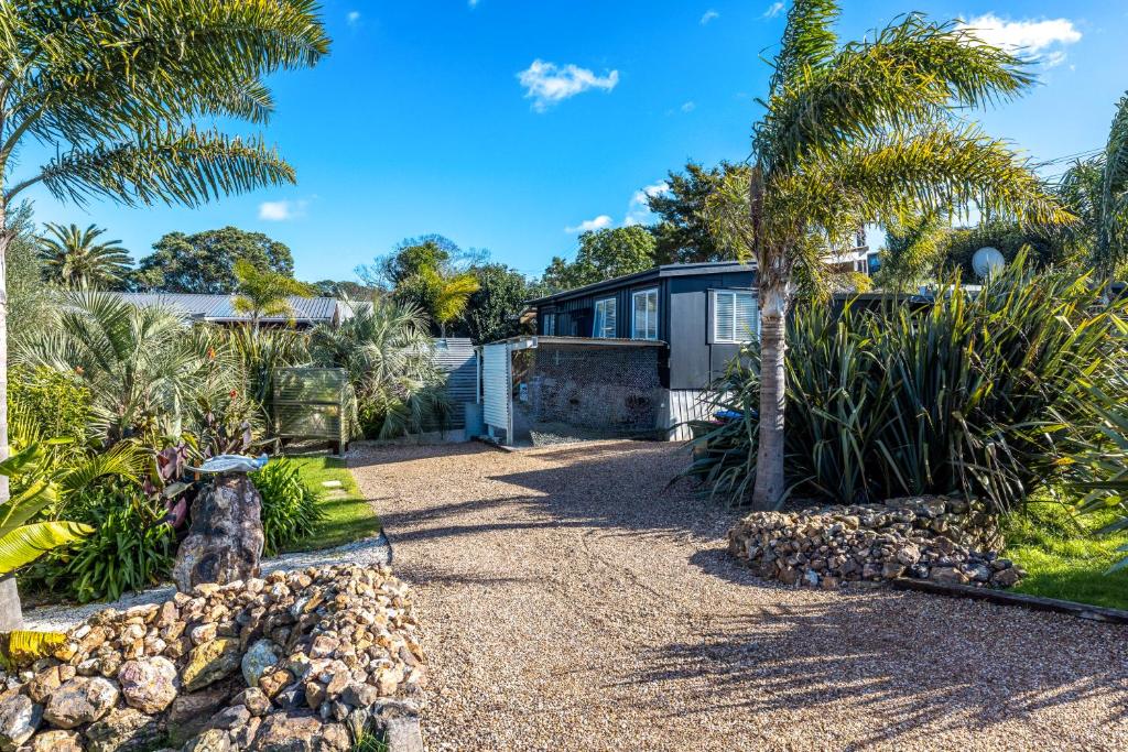 a house with palm trees and a gravel driveway at Welcome Cottage in Oneroa
