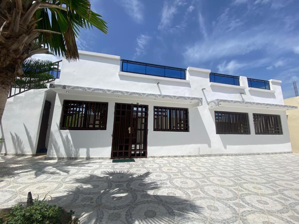 une maison blanche avec un palmier en face dans l'établissement Villa OMARI Situé à Saly Portudal Villa 2 Chambres bien équipés proche de tout, à Saly Portudal