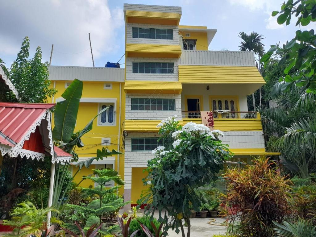 ein gelbes Gebäude mit Bäumen davor in der Unterkunft Balurghat Hotel KOKORO Farmhouse in Bālurghāt