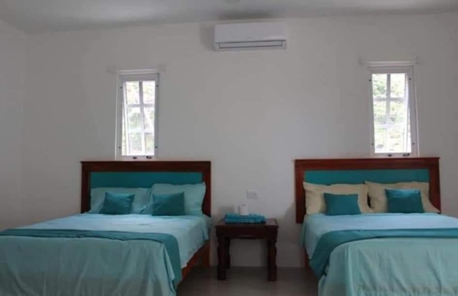 two beds in a white room with two windows at Departamentos y habitaciones Sak Naj in Telchac Puerto