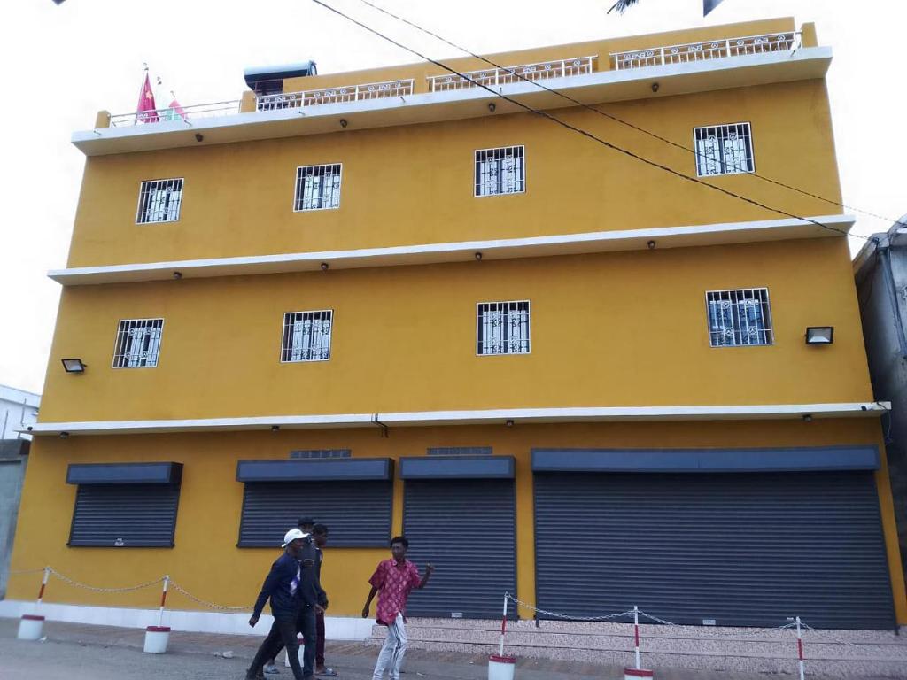 two people walking in front of a yellow building at Hôtel restaurant CMG in Ilakaka