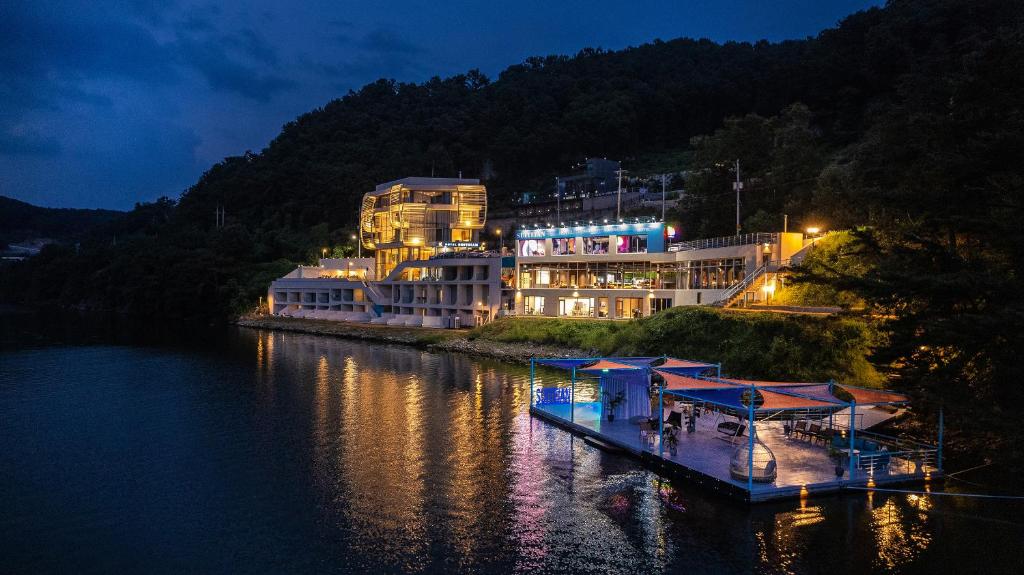 Gapyeong Suiteian Hotel&Resort في كابيونغ: مبنى كبير على جانب النهر في الليل