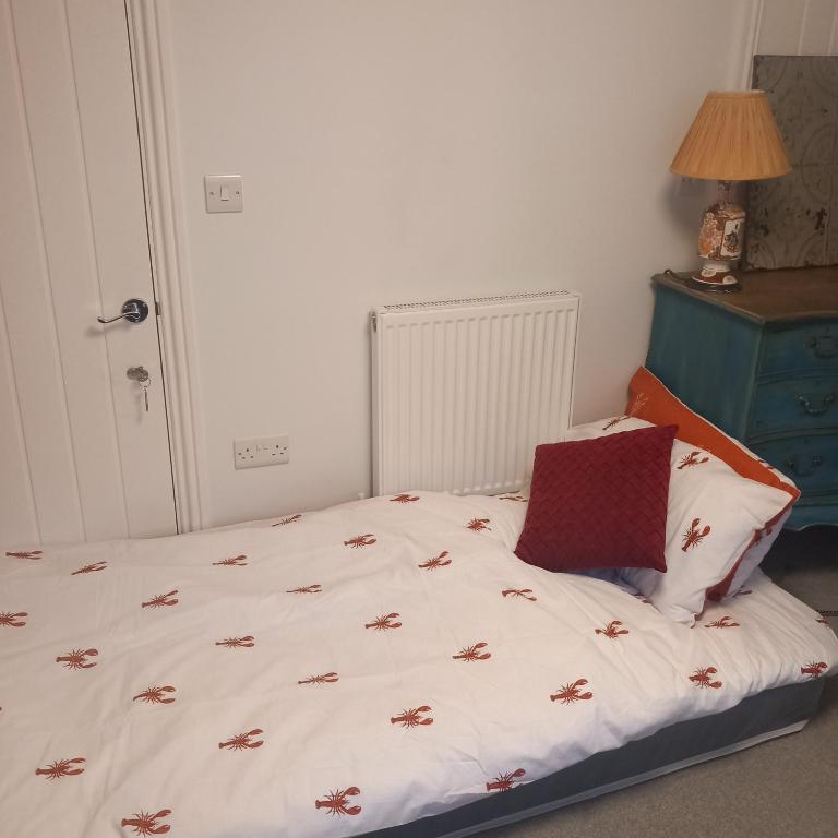 a bed with a white comforter and a red pillow at Hideaway cottage - Studio ground floor with toilet and sink in Sandgate