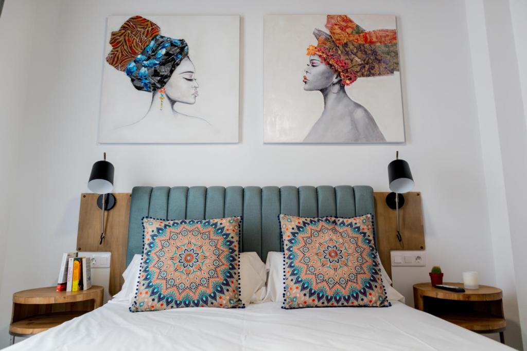 Calma Suites في إشبيلية: غرفة نوم بسرير ومخدات وصور على الحائط