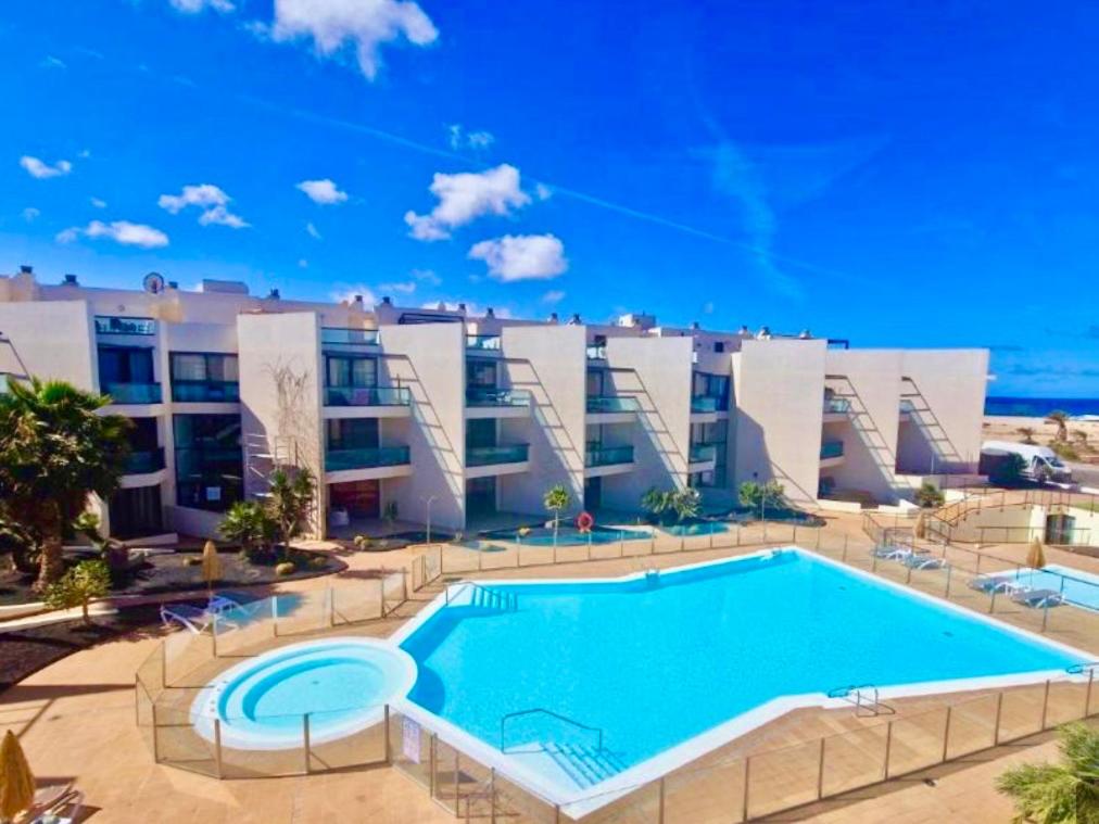 a large swimming pool in front of a building at Apartamento Villa Bruno con vistas al mar, primera línea de playa in Cotillo