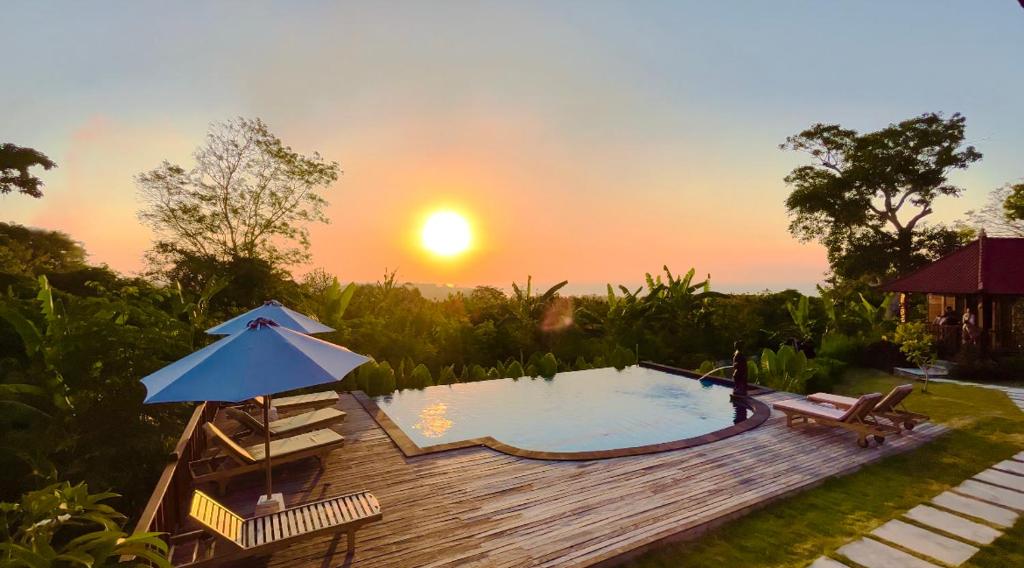 a pool with an umbrella and a sunset in the background at Sunset Hill Lembongan in Nusa Lembongan