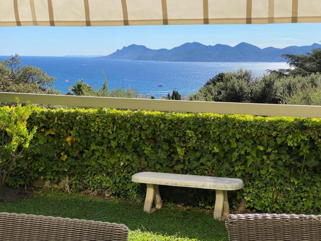 a bench sitting in front of a hedge with the ocean at Cannes la Californie, appartement-villa LE SAINT GEORGES, avec grand jardin et vue mer in Cannes