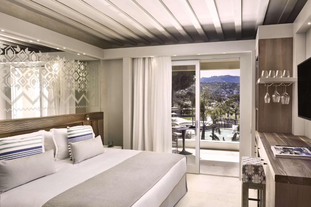 a bedroom with a large bed and a balcony at 7Pines Resort Sardinia - A Destination By Hyatt in Baja Sardinia