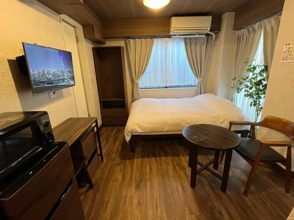 東京にあるCozy inn Oyamaのベッド、テーブル、テレビが備わる小さな客室です。