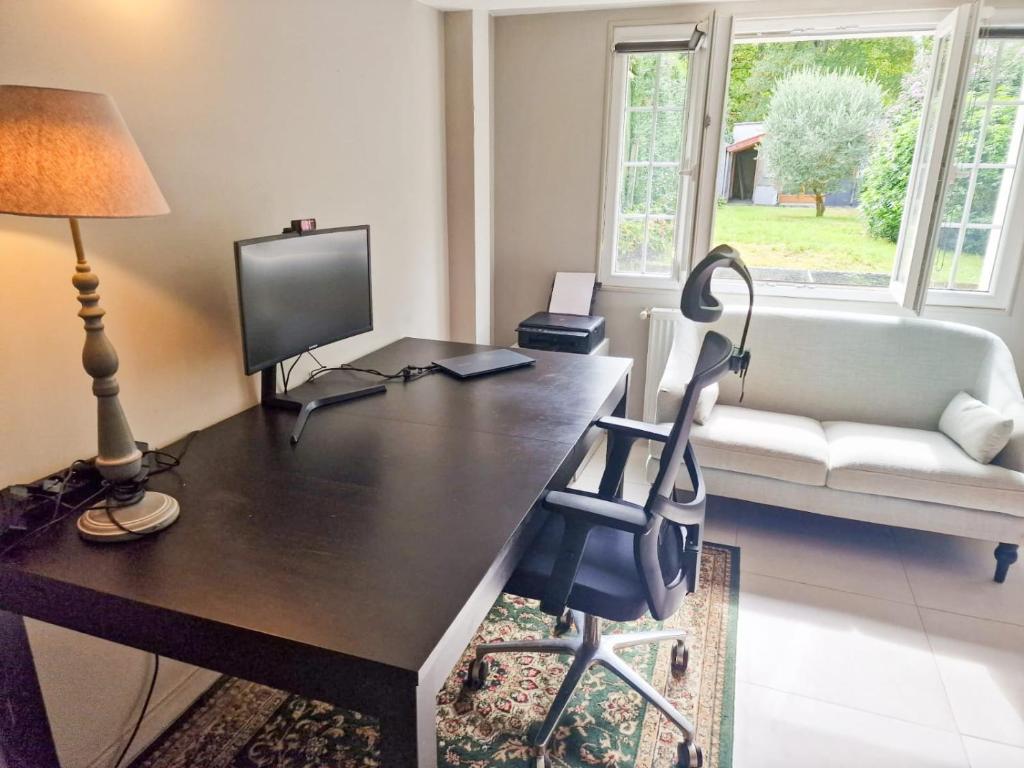 ein Wohnzimmer mit einem Schreibtisch, einem TV und einem Stuhl in der Unterkunft Villa Nature entre Paris et Versailles in Marnes-la-Coquette