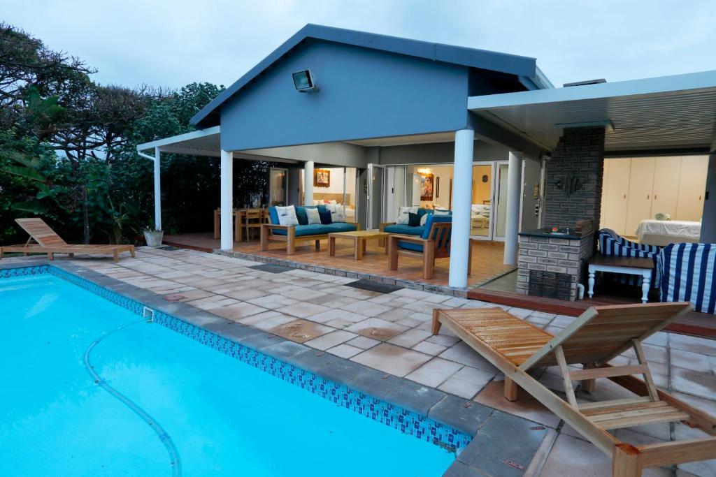 a swimming pool with chairs and a house at Fiddlewood Beach House in Port Shepstone
