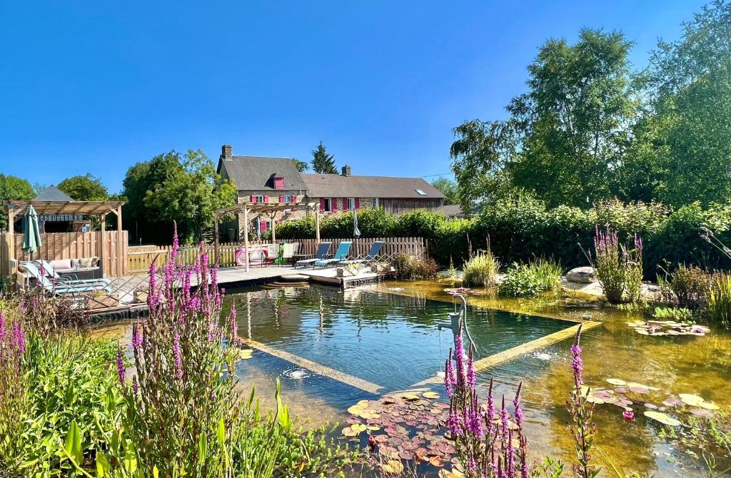 a pond in front of a house with purple flowers at Greener Pastures - Normandy Self Catering Gites in La Chapelle-Engerbold