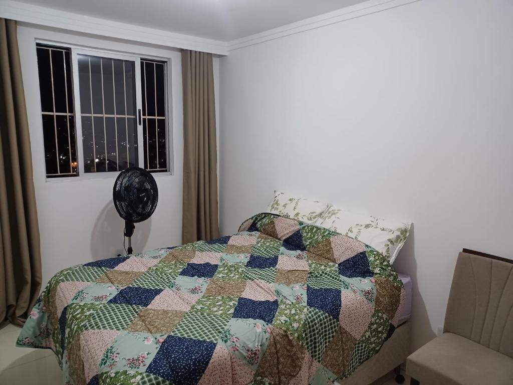 a bedroom with a quilt on a bed with a window at Aluga-se quarto em apartamento in Ipatinga