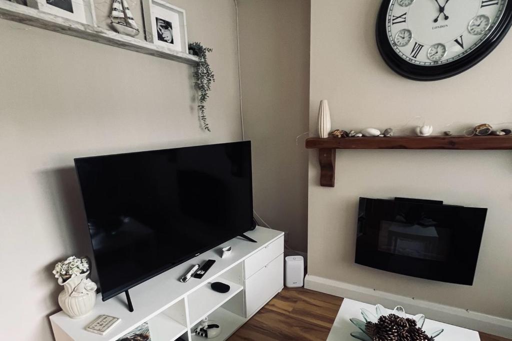 a living room with a flat screen tv and a clock at Cosy one bed apartment in Carnlough in Ballymena