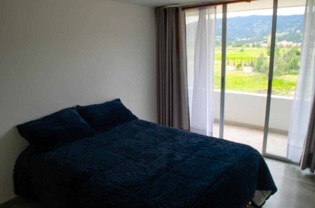 1 dormitorio con cama azul y ventana grande en Apartahogar, en Paipa