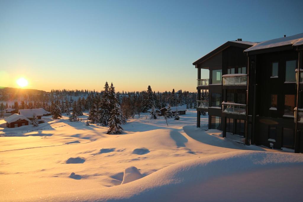 a lodge in the snow with the sun setting in the background at Beautiful penthouse with panoramic view at Sjusjøen in Ringsaker
