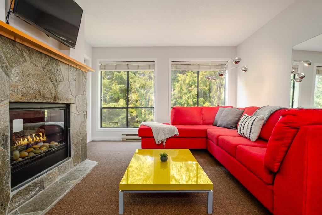 a living room with a red couch and a fireplace at Steps to the Ski Hill with Rooftop Hot Tub by Harmony Whistler in Whistler