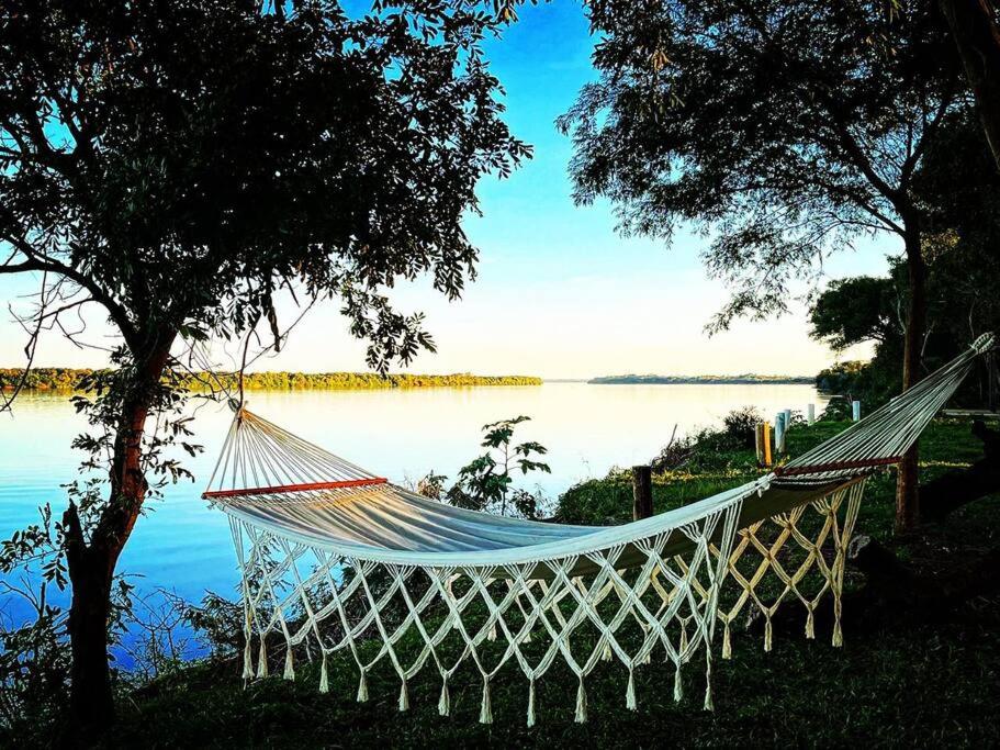 a hammock hanging between two trees next to a lake at Pura Vida in Yapeyú