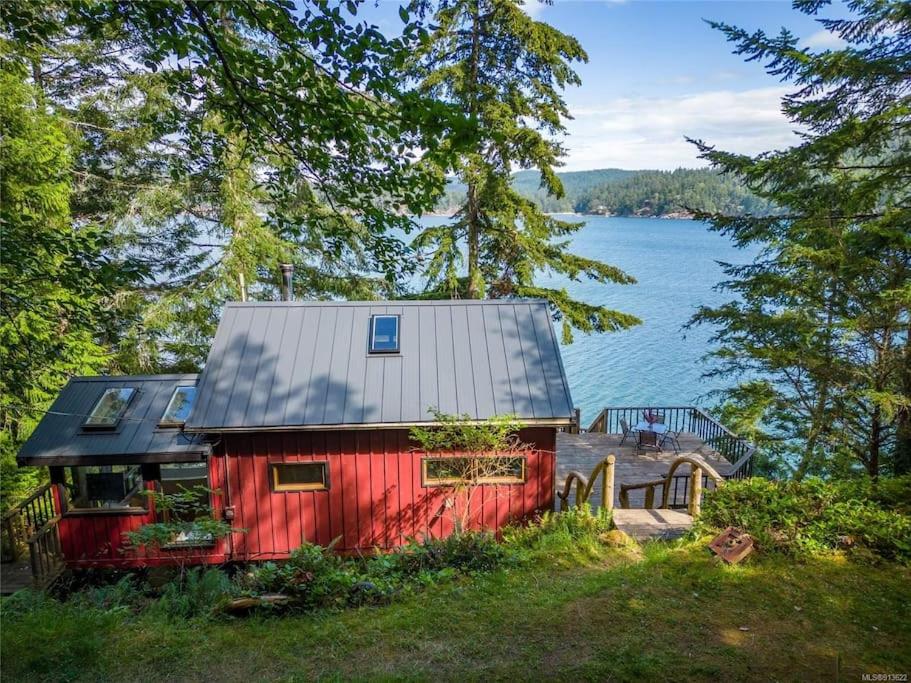 a red house with a silver roof next to the water at The Salish Sunset Cabin in Pender Island