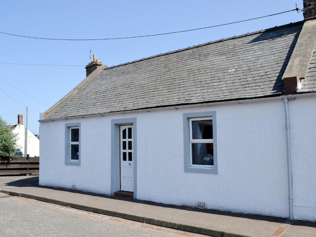 a white house with a gray roof on a street at Creel Cottage in Auchmithie