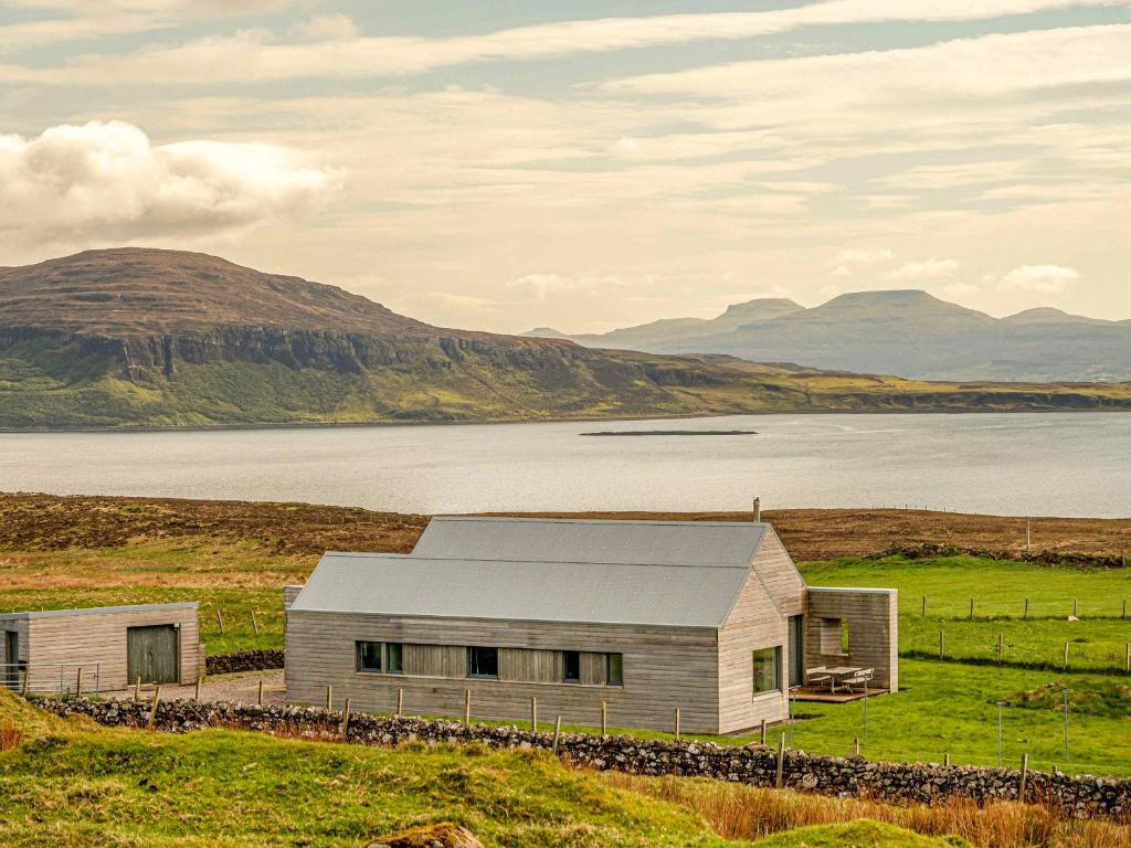 a barn in a field next to a body of water at The Two Byres in Trumpan