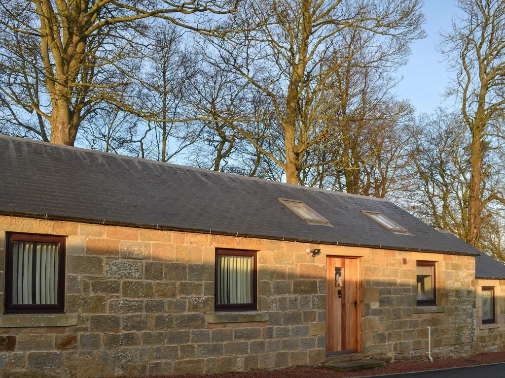 a stone building with a black roof and a door at Heckley Stable Cottage in Alnwick