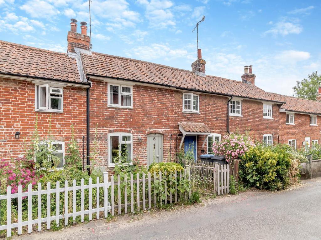 ein rotes Backsteinhaus mit einem weißen Zaun in der Unterkunft Heartwarming Cottage in Wickham Market