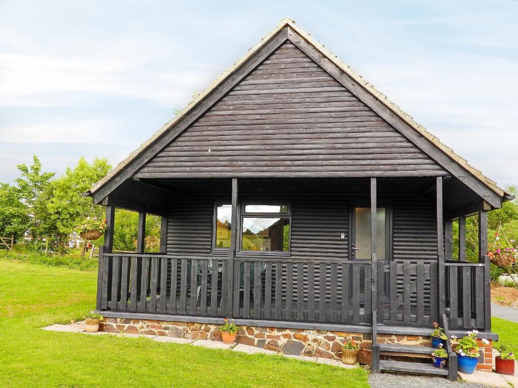 a black cottage with a porch on a lawn at Primrose Lodge - Uk13447 in Halwill