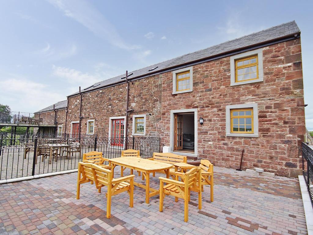 a wooden table and chairs in front of a brick building at Meadow Lodge-e4105 in Aspatria