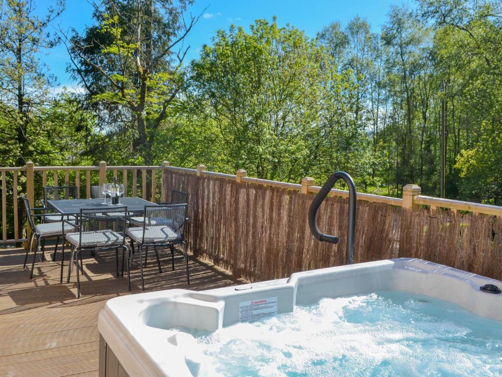 a hot tub on a deck with a table and chairs at Maple Lodge in Otterburn