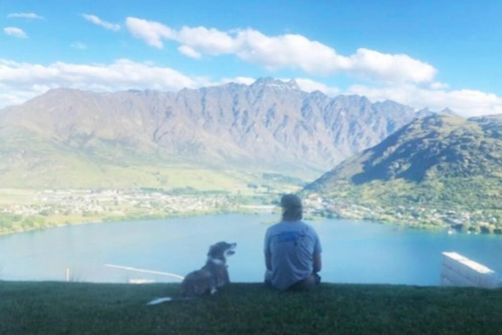 Ein Mann und sein Hund sitzen auf einem Hügel mit Blick auf einen See. in der Unterkunft Views on Florence in Queenstown